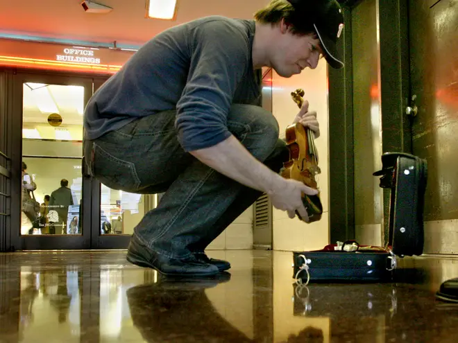 Joshua Bell agachado ao lado do estojo do violino na estação de metrô de Washington